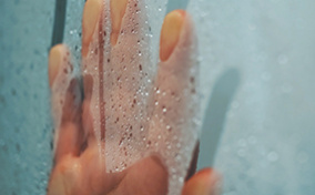 A hand streaks down a fogged up window covered in condensation.