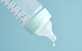 An empty formula bottle tips downward with a single drop of milk falling from the nipple.