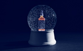 A light shines on the side of a snow globe with a bottle of whiskey inside as it sits in the dark.