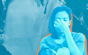 A woman holds her newborn against her chest as she holds the bridge of her nose.