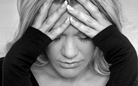A black and white photo shows a distressed woman wither her forehead in her hands.