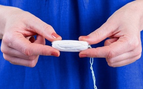 A person holds a tampon in two hands with their fingers. 