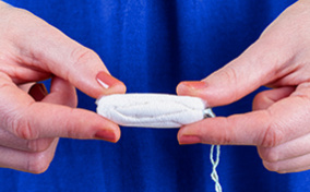 A person holds a tampon in two hands with their fingers. 