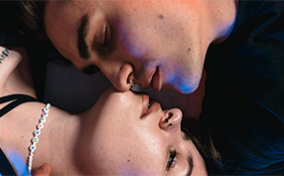 Two people lying in opposite directions press their faces together with their eyes closed.