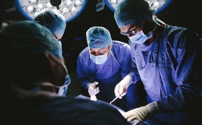A team of surgeons and doctors lean over a person as surgery is performed on them.