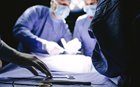 Doctors in medical gear crowd around a tray with surgical instruments on it.