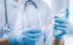 A gloved doctor holds a needle in their hands. 
