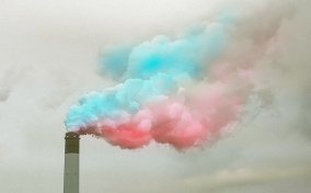 Blue and pink smoke billows out the top of a smoke stack. 