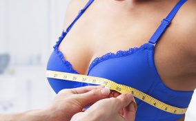 A person measures the bust of a woman in a blue bra.