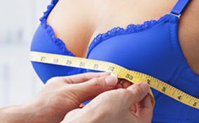 A person measures the bust of a woman in a blue bra.