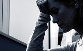 A black and white photo shows the profile of a person with their head in their hand.