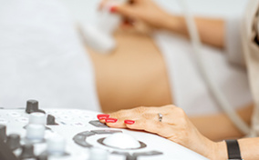 A woman lays back as an OB-GYN uses an ultrasound machine to view her abdomen.