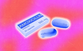 A box of amoxicillin lays beside two erythromycin pills.