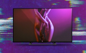 A TV shows a nude woman with her crossed over her body as a purple light shines behind her.