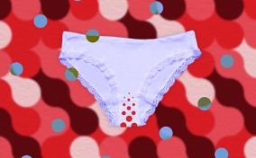 Lavender underwear with red dots in the crotch area lays against a red patterned background.