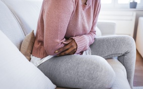 A woman holds her stomach while sitting on the sofa.