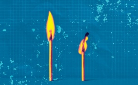 A match is lit next to another that is half-burnt against a teal background.
