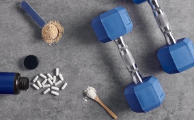 Vitamins and supplements in powder- and pill- forms lay on the ground next to two dumbbells.