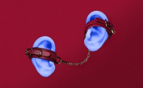 A pair of leather handcuffs are attacked to two light blue ears against a red background.