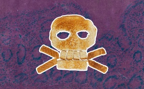 A piece of bread in the shape of a skull and cross bones is layered on a pink and purple marbled background.