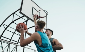 Two men are playing basketball outside.