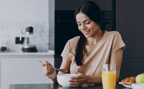A woman sits down at a kitchen counter eating a fiber-rich breakfast.