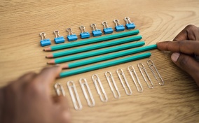 A pencil is being slid into a straight line of other pencils in between a row of paperclips and a row of binder clips.
