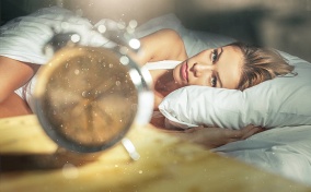 A woman looks at a clock on her nightstand.