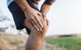 A man holds his right knee in pain and rubbing it.