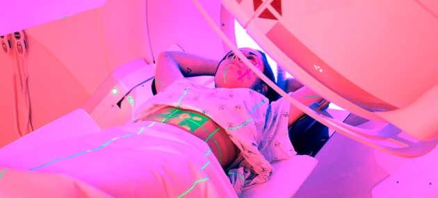 A woman lies down under a radiation machine.