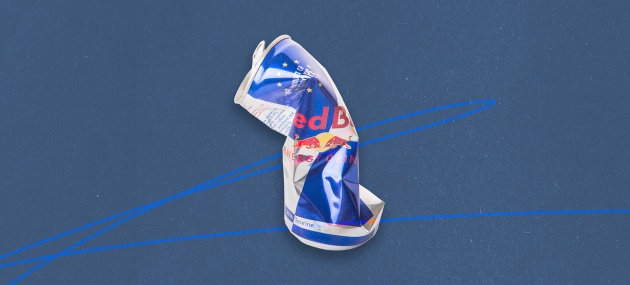 A can of Red Bull that has been squeezed and crunched is against a blue background.