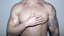 bare torso of a man on a gray background as he touches one side of his chest