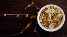 A small bowl of pumpkin seeds sits on top of a branch growing red and yellow berries.