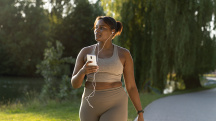 A black woman in activewear walks along a path outside while listening to music.