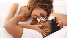 man lays on bed about to kiss a woman on top of him as they cuddle and smile