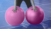 grayscale man holding two pink yoga balls in gray gym