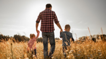 A father walks through a field holding hands with his two children.